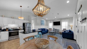 A modern kitchen with stainless steel appliances, a dining area with a round table and chairs, a blue sofa set, and a chandelier. - A Sunshine Daydream | 30A Home w/ Community Pool + Outdoor Shower (Santa Rosa Beach)