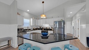 A modern kitchen with white cabinetry, a stainless steel refrigerator, a central island with stools, and a pendant light. - A Sunshine Daydream | 30A Home w/ Community Pool + Outdoor Shower (Santa Rosa Beach)