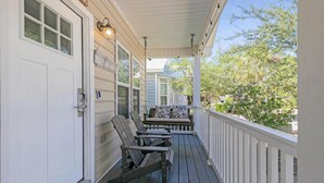 A covered porch with two Adirondack chairs and a small table, a white door, and a window with a view of greenery. - A Sunshine Daydream | 30A Home w/ Community Pool + Outdoor Shower (Santa Rosa Beach)