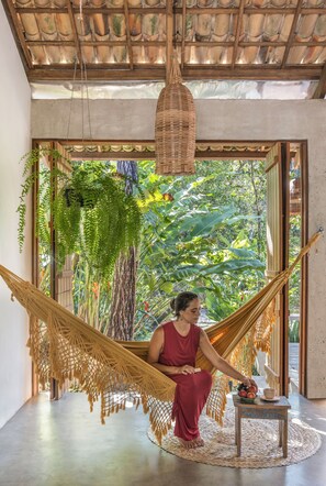 A hammock chair in a room with a view of lush greenery. - Casa Canoa (Maraú)