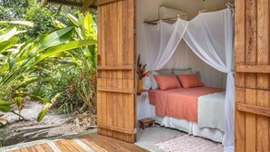 A wooden room with a bed, a small stool, and a white canopy bed.