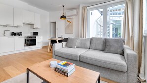 Un apartamento moderno con kitchenette, un sofá gris, comedor y un amplio ventanal con cortinas.