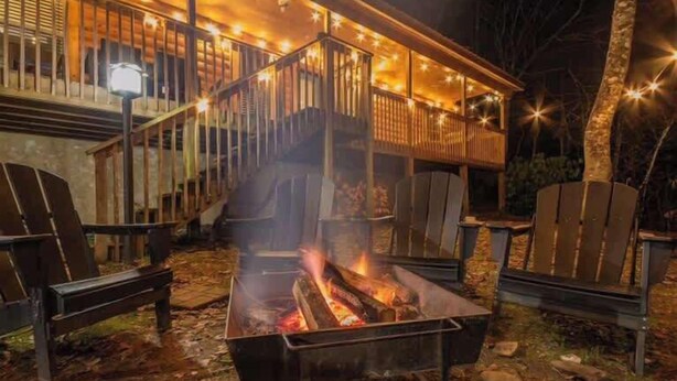 A covered outdoor seating area with a fire pit, wooden chairs, and a staircase leading to an upper deck. - High Johnny’s Hideout • Private Hot Tub Retreat (Sevierville)