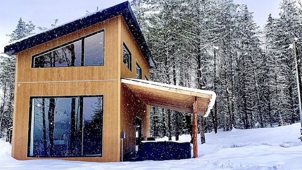 A modern wooden cabin with large windows and a covered porch, surrounded by snow and trees. - Valley view north arm#spas#outdoor fireplace#nature#guaranteed fun (Saint-Raymond)