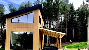 A modern two-story house with large windows, a wooden exterior, and a covered patio area. - Valley view north arm#spas#outdoor fireplace#nature#guaranteed fun (Saint-Raymond)