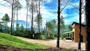 A modern house with a large deck, surrounded by tall trees and a grassy hill. - Valley view north arm#spas#outdoor fireplace#nature#guaranteed fun (Saint-Raymond)