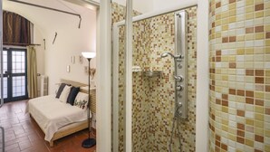 A bedroom with a bed, a bedside table, a lamp, and a shower area with tiled walls. - L'Antica Concia di Santa Croce - Sweet Dreams in Florence (Firenze)