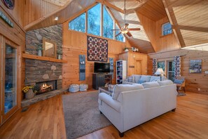 Cozy living room with a stone fireplace, comfortable sofa, and large windows.