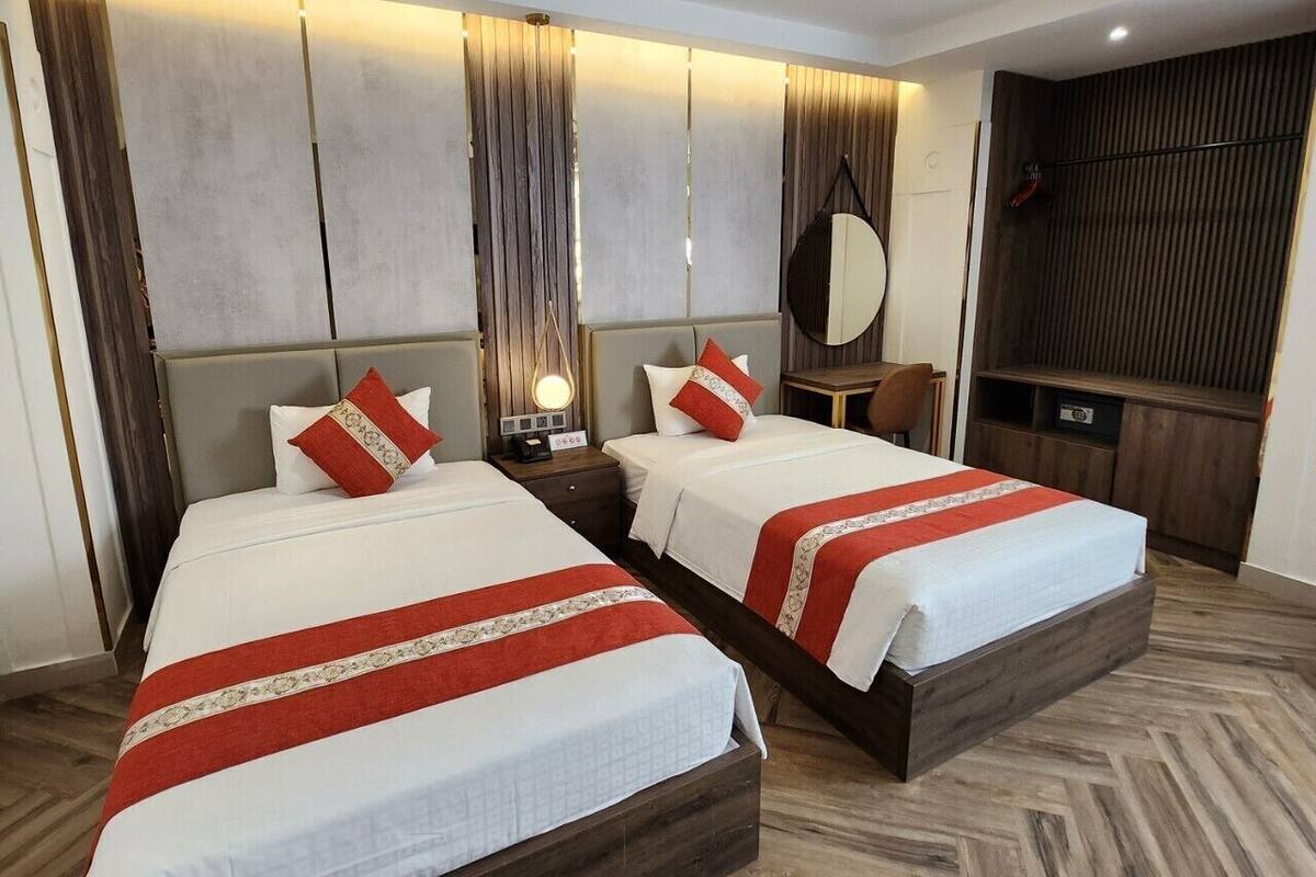 Une chambre d’hôtel avec deux lits, une table de chevet avec une lampe, un miroir, une télévision et un plancher en bois.
