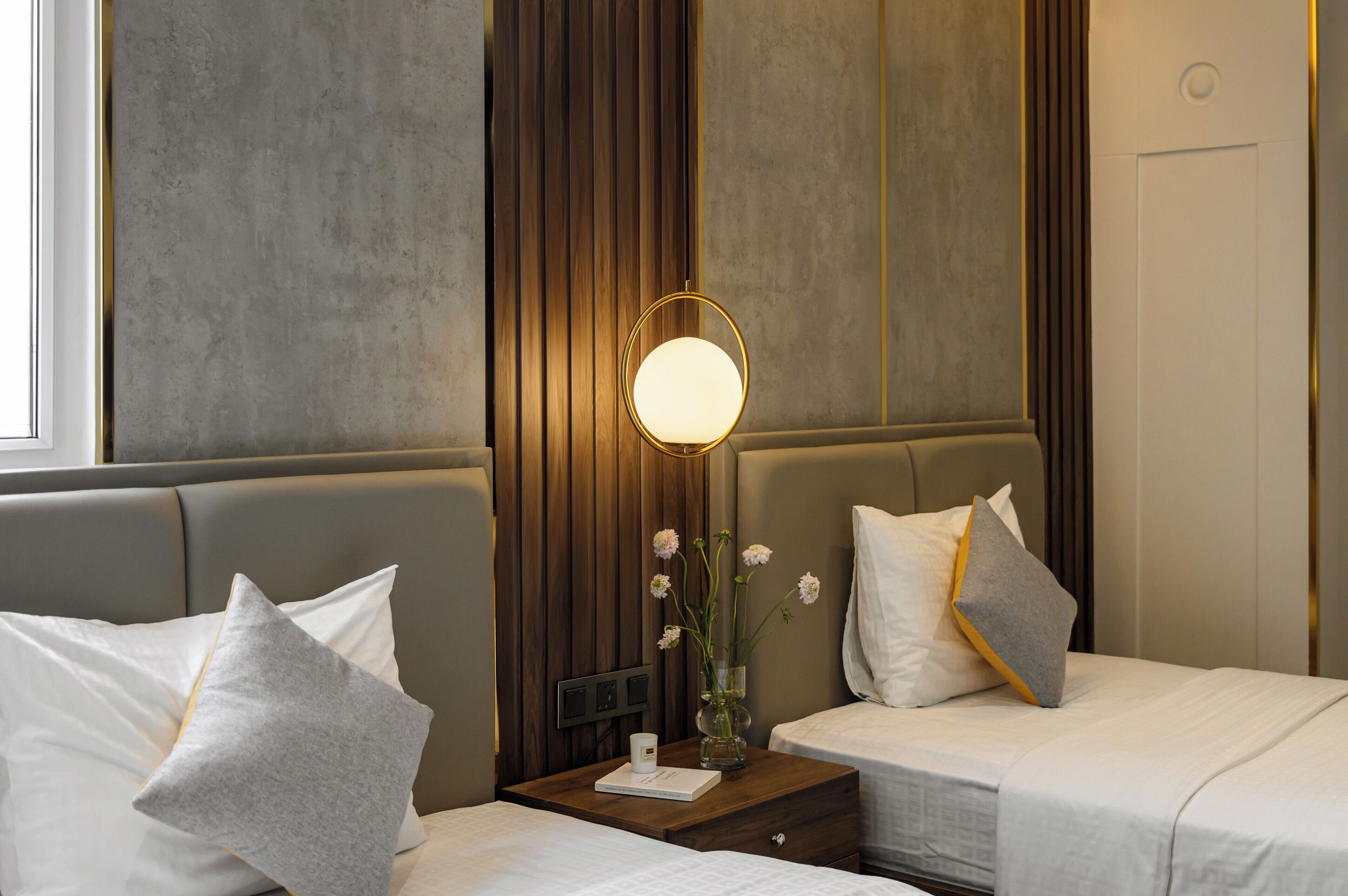 A hotel room with two beds, a nightstand with a lamp, and a vase with flowers.