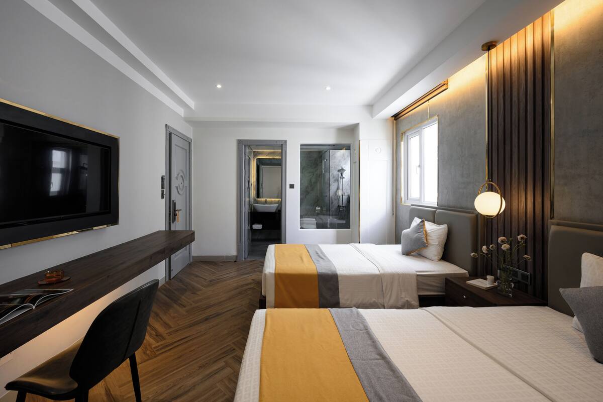 Une chambre d’hôtel moderne dotée d’une télévision à écran plat, d’un bureau, de deux lits, d’une grande fenêtre et d’un plancher en bois.