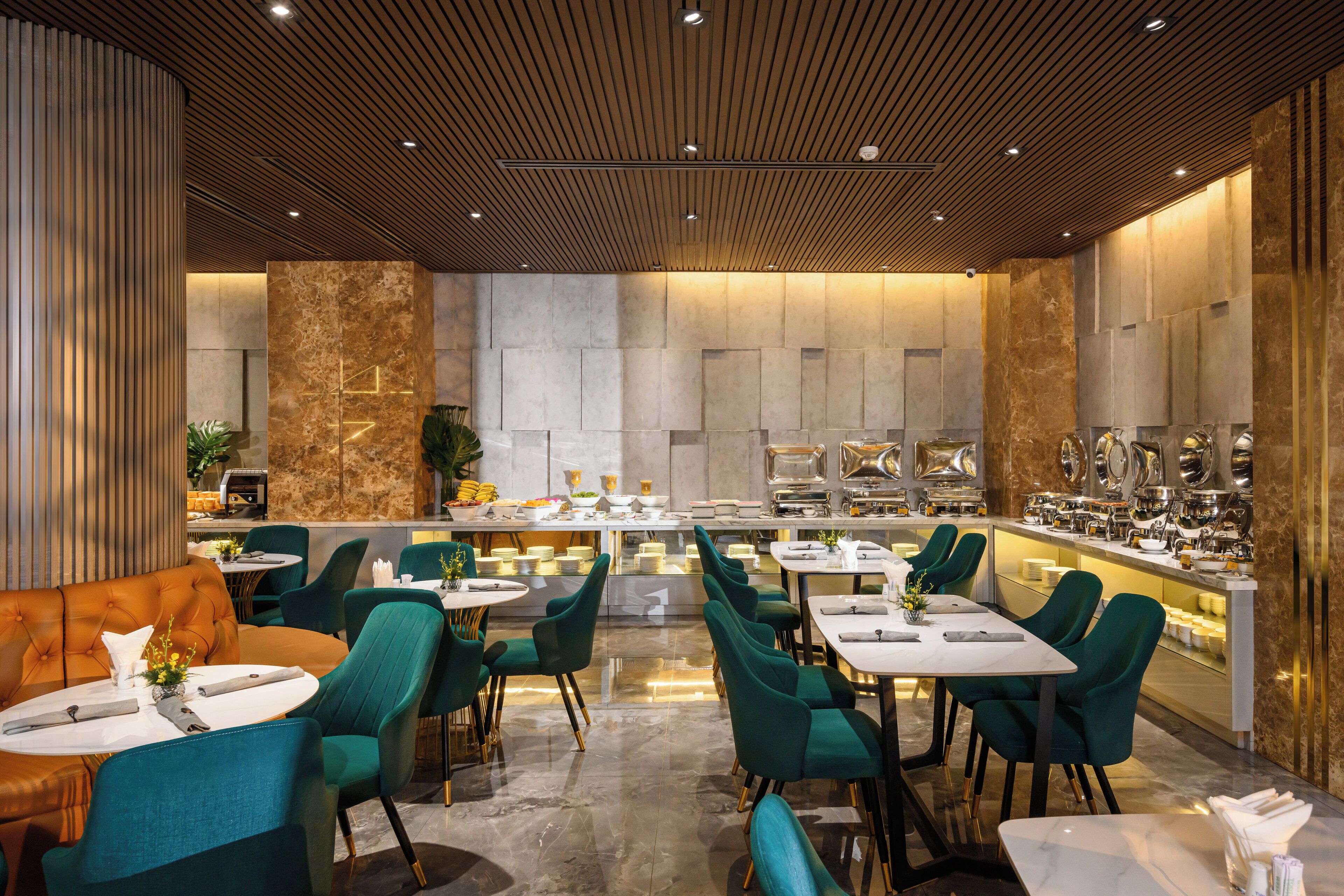 A modern restaurant with a bar area, green upholstered chairs, and a marble floor.