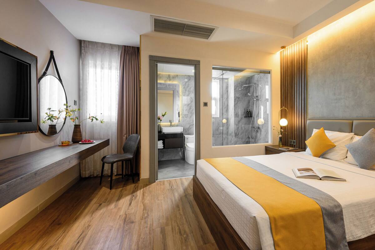 Une chambre d’hôtel moderne, dotée d’un grand lit, d’un bureau et d’une salle de bain visible à travers une porte ouverte.