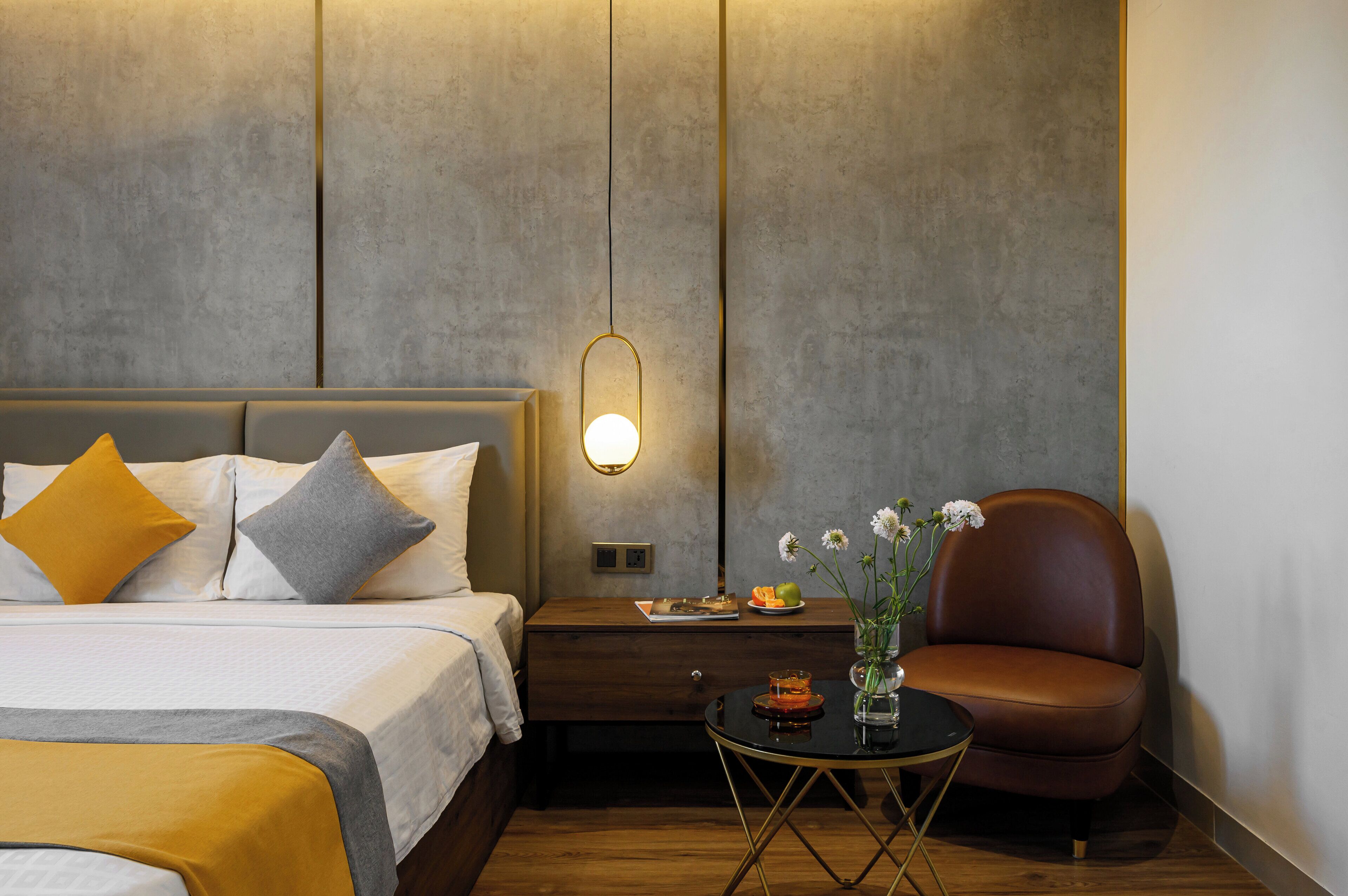 A modern hotel room with a bed, a nightstand, a chair, and a small table with a vase of flowers.