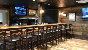 A bar area with a long counter, multiple bar stools, a television mounted on the wall, and a bar stocked with bottles. - Hummingbird Hideaway in Connestee Falls (Brevard)