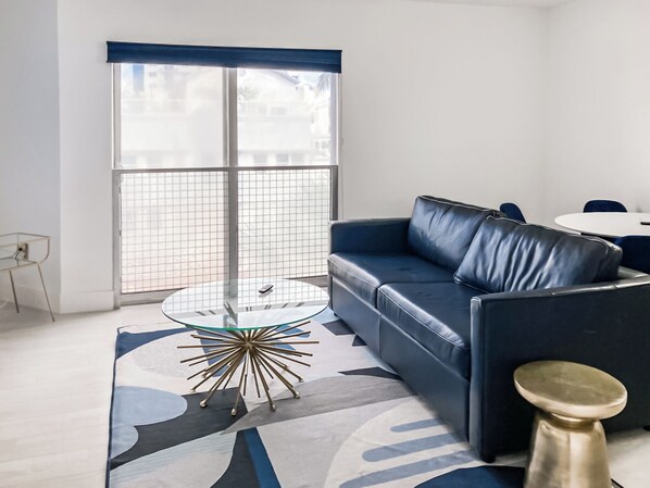 Ein modernes Wohnzimmer mit einem blauen Ledersofa, einem Glastisch mit goldener Basis und einem runden Seitentisch aus Gold.