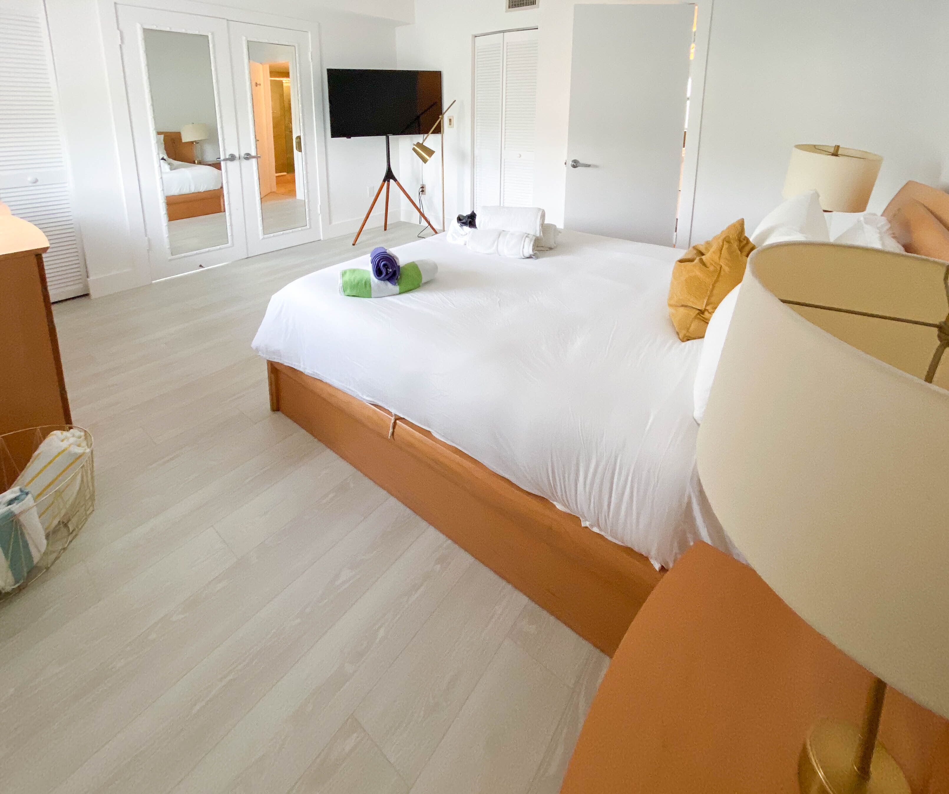 Et hotelværelse med en stor seng, et fjernsyn på et stativ, et klædeskab og et natbord.