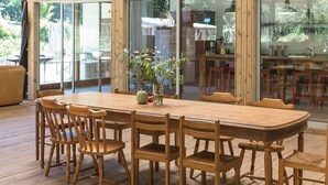 Un vaste espace dédié à la salle à manger, avec une grande table et des chaises en bois, entouré de portes vitrées donnant sur un jardin.