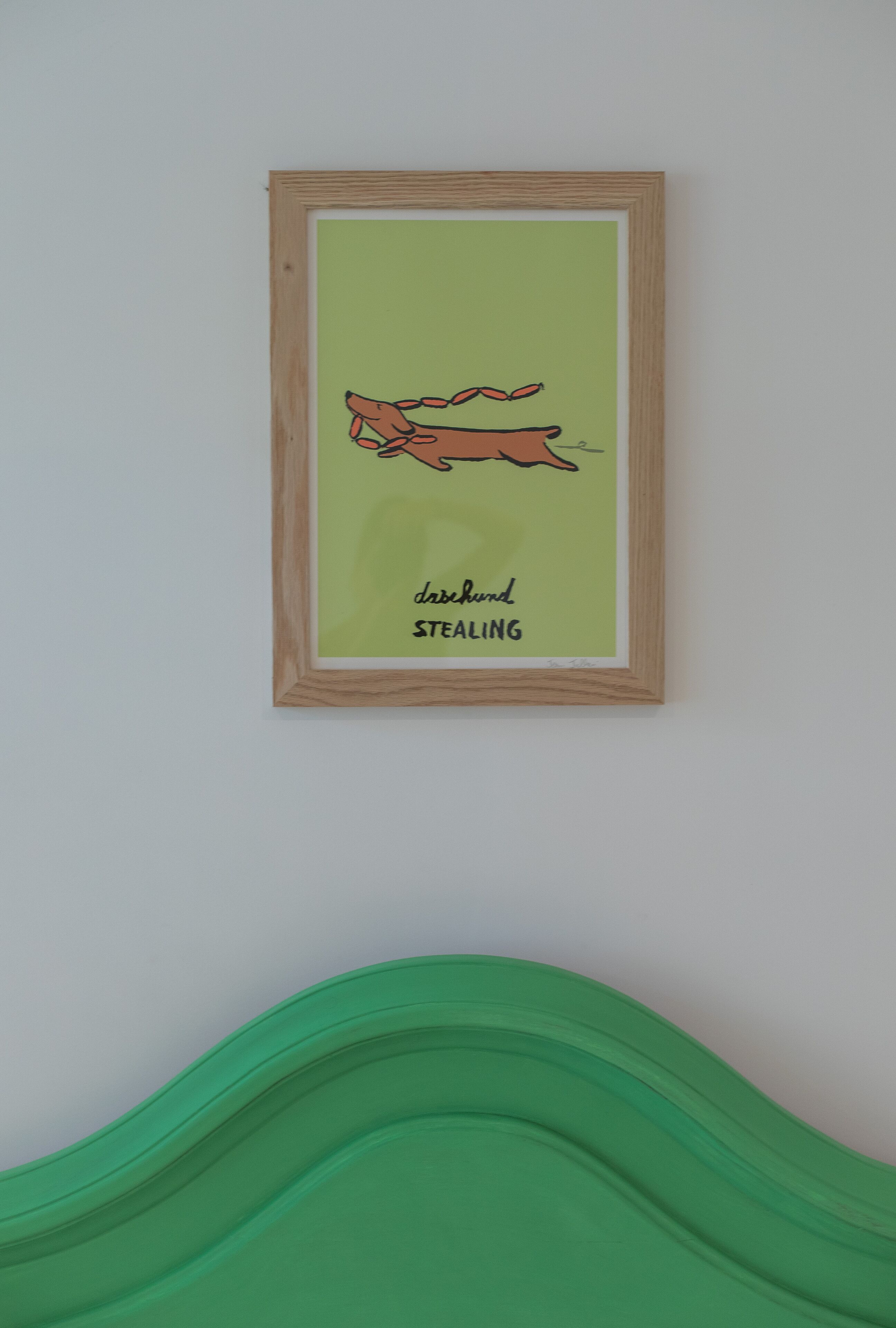 Une œuvre d’art encadrée représentant un chien et portant l’inscription « DACHSHUND À LA CHASSE » sur un fond vert clair.