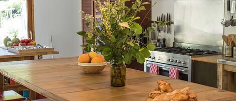 A kitchen with a wooden island, red stools, hanging pendant lights, a stove, and a fruit bowl.