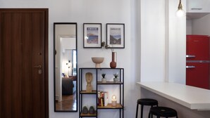 Une cuisine moderne avec un plan de travail blanc, un réfrigérateur rouge et une étagère métallique noire agrémentée d’objets décoratifs.