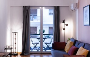 Ein modernes Wohnzimmer mit einer Couch, einer Stehlampe und Blick durch eine Glastür auf einen Balkon.