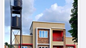 A two-story building with a water tower, a red door, and a brick facade. - Immaculate 3-Bed House in Owerri with garden (Owerri)