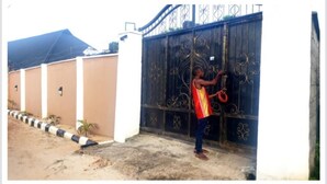 A person standing in front of a large, ornate metal gate. - Immaculate 3-Bed House in Owerri with garden (Owerri)
