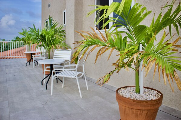 A terrace with a table and chairs, potted plants, and a building in the background.