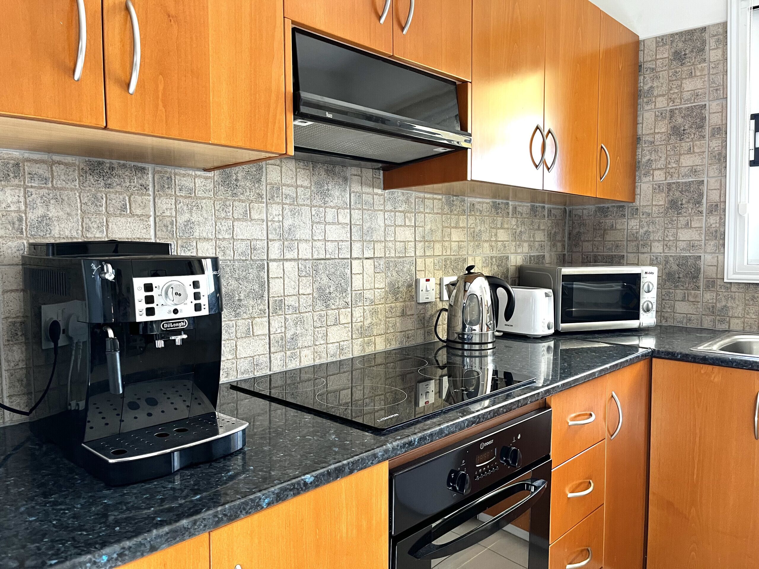 A modern kitchen with wooden cabinets, a built-in microwave, a coffee machine, and a kettle.