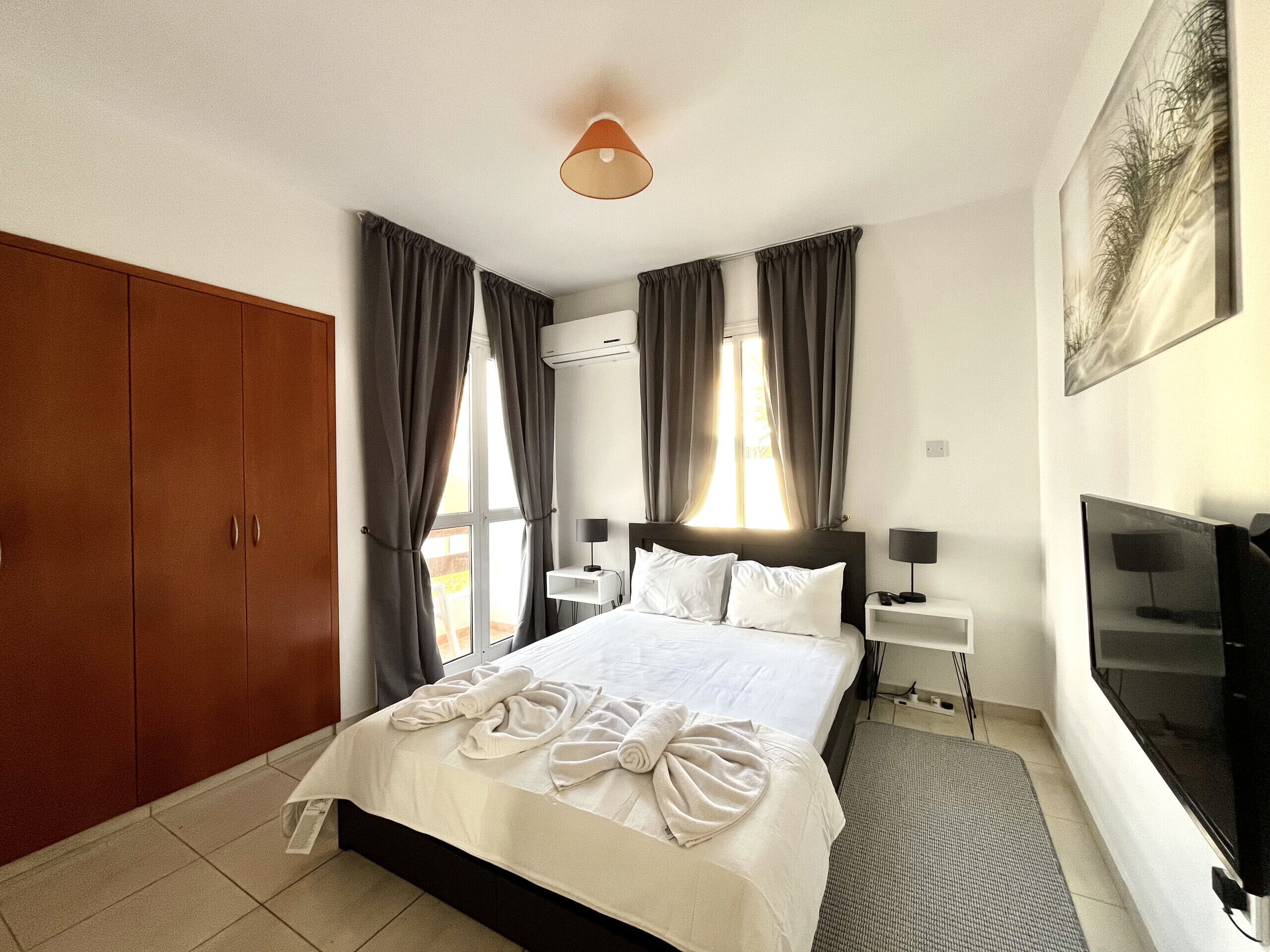 Une chambre d’hôtel avec un grand lit, une armoire, un bureau avec une lampe, une télévision et un tableau au mur.