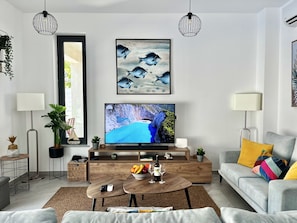 A modern living room with a flat-screen TV, wooden coffee table, grey sofa, and decorative plants.