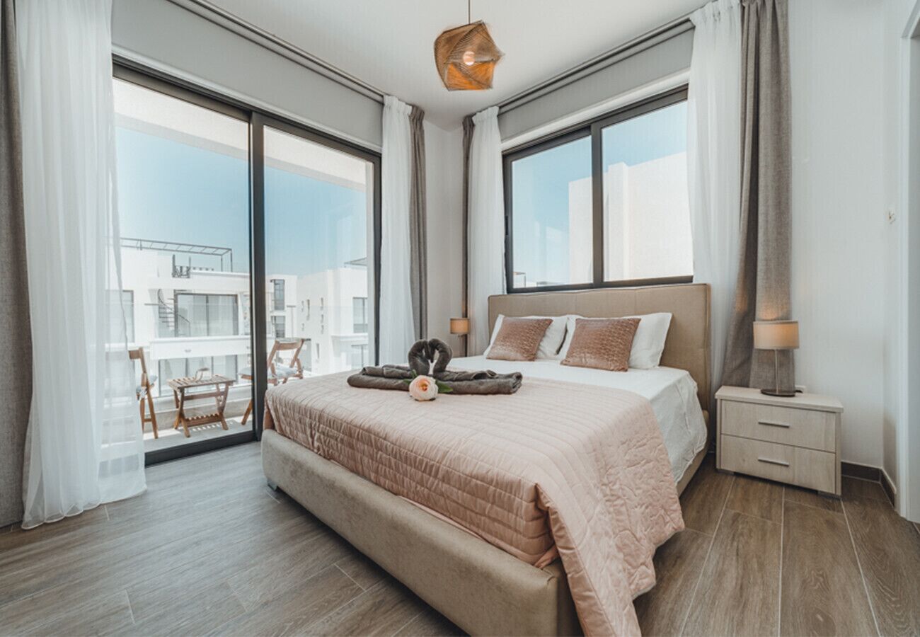 A modern bedroom with a large bed, a nightstand, and a view of the city through large windows.