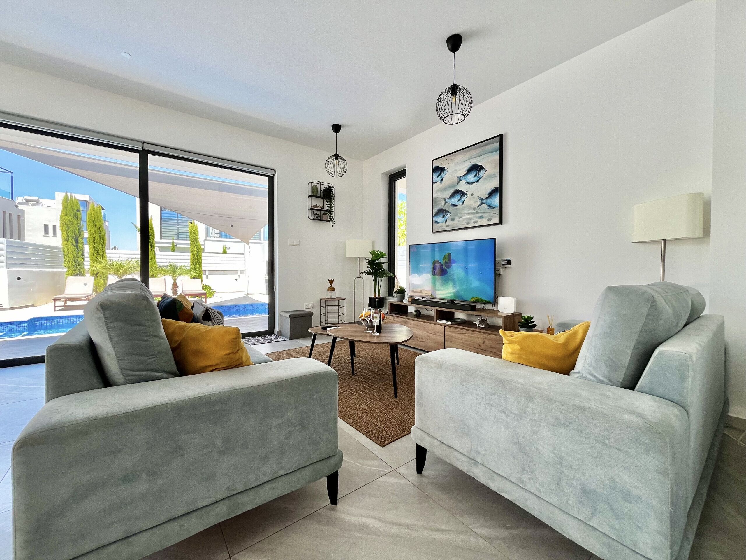 A modern living room with a large TV, comfortable seating, and a view of a swimming pool.