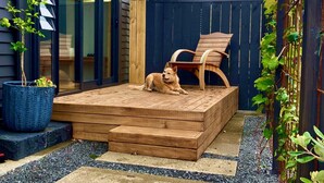 A wooden deck with a dog, a chair, and a potted plant.