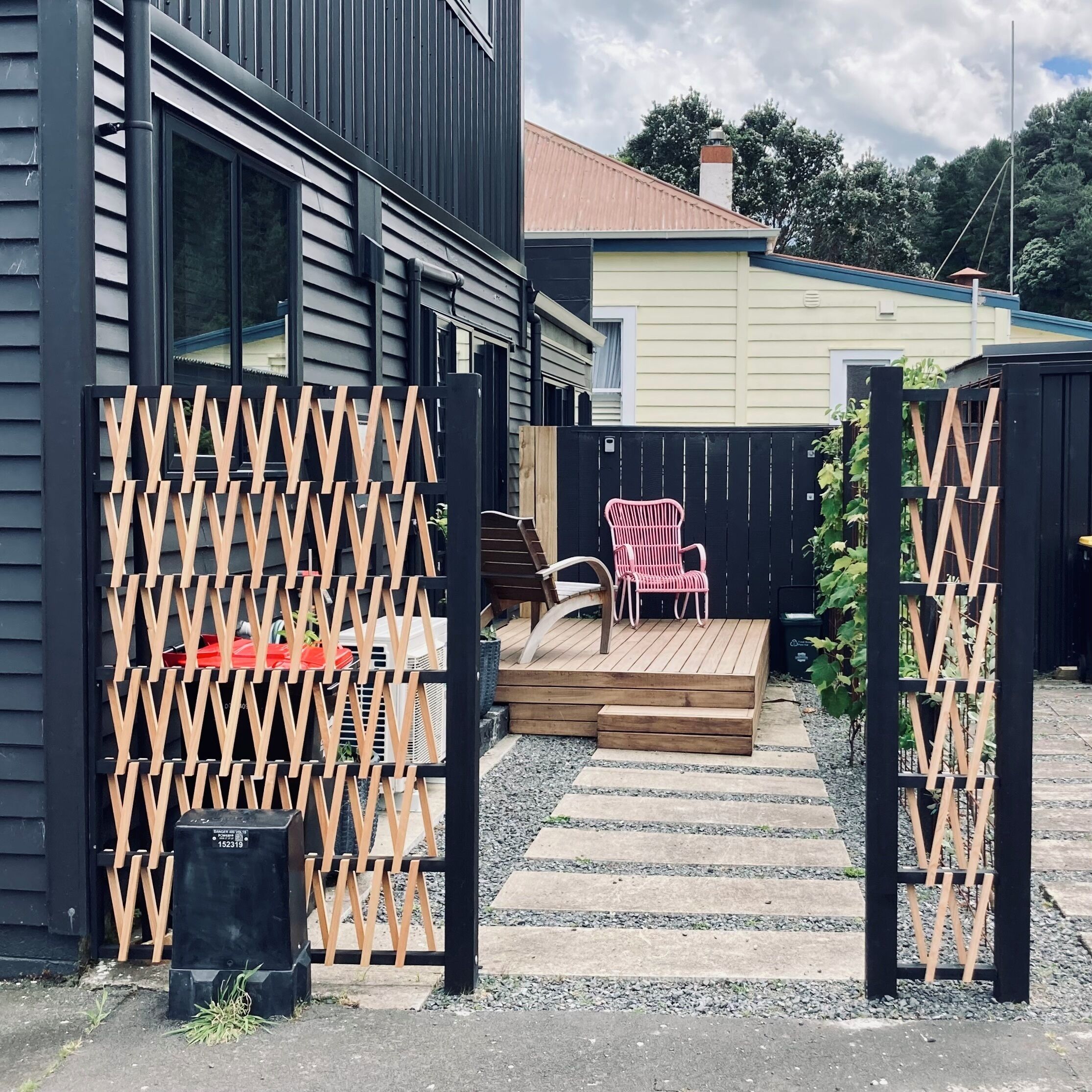A modern house with a wooden deck, a red chair, and a black fence.