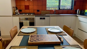 A modern kitchen with a dining table set for two, equipped with a microwave, oven, and a window with blinds.