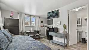 A compact room with a bed, a desk, a TV, a microwave, and a small kitchenette.
