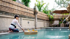 Zona junto a la piscina con valla de bambú, cesta de mimbre con bebidas y una estatua.