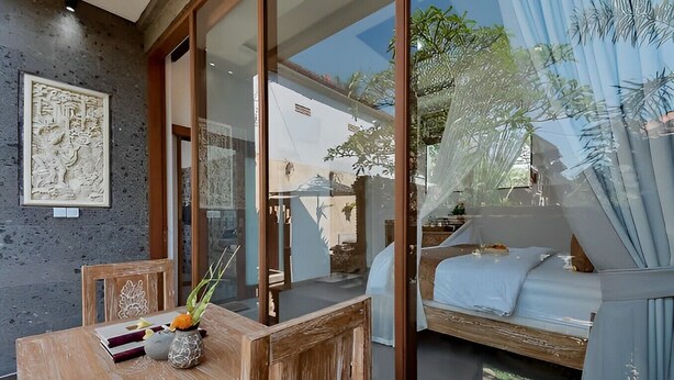 Una habitación moderna con una mesa de madera, una cama con colcha blanca y un ventanal con vistas al exterior.