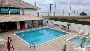 A swimming pool area with two pools, lounge chairs, and a covered seating area. - CASABLANCA Praia Hotel (Peruíbe)