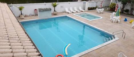 Une piscine avec des marches descendant vers l’eau, entourée de chaises longues blanches et de parasols.