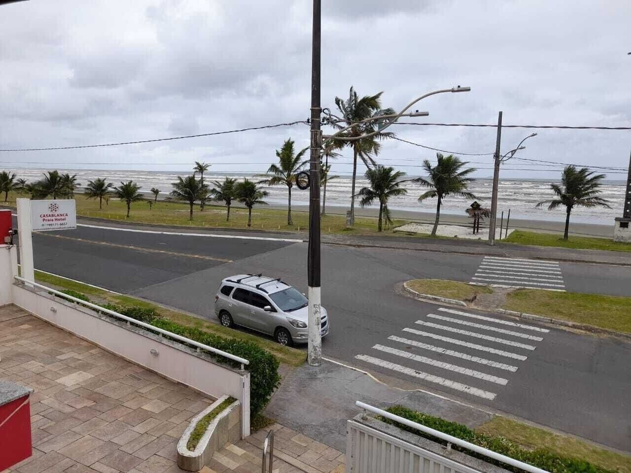 Une vue de rue avec une voiture garée près d’un passage pour piétons, des palmiers et une plage en arrière-plan.
