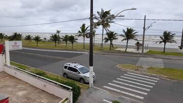 Une vue de rue avec une voiture garée près d’un passage pour piétons, des palmiers et une plage en arrière-plan.