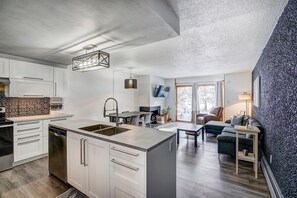 Une cuisine moderne avec des meubles blancs, un îlot central doté d’un évier et un coin repas avec une table et des chaises.