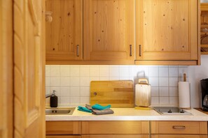 A kitchen with wooden cabinets, a sink, a cutting board, a kettle, and a roll of paper towels.