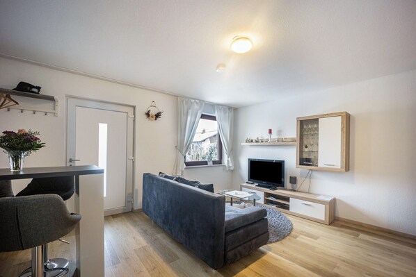Een moderne woonkamer met een bank, een televisie, een salontafel en een raam met gordijnen.