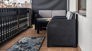 Een balkon met een rieten bank, een klein tafeltje en een kamerkleed met dessin.