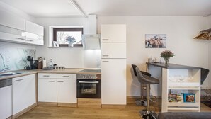 Een moderne keuken met witte kastjes, een inbouwoven, een koffieapparaat en een bar met krukken.
