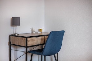 Ett hörnskrivbord med en lampa, en stol och en liten dekorativ detalj på väggen.